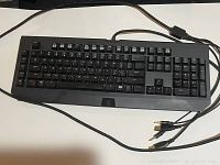Photo of full keyboard showing standard layout with connected cables including USB and audio connectors on white background.