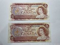 Front view of two 1974 Canadian two dollar bills showing Queen Elizabeth II and denominations with prefixes ARC6825024 and ARE7229930.