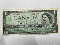Front side of the Canadian one dollar bill from 1867-1967 Centennial of Confederation showing Queen Elizabeth II and denomination.