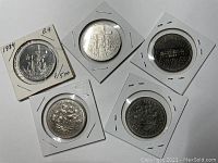 Top view of the five nickel dollar coins showing the reverse side designs including a voyageur canoe scene, the Parliament building, and floral emblematic designs. Coins are protected in white cardboard and plastic holders.