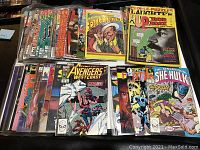 Overall view of mixed comic books with multiple Marvel and DC titles, including Avengers West Coast and Laughter magazines in protective sleeves.