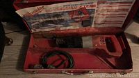 Photo of Milwaukee reciprocating saw inside red metal carrying case showing tool and internal case label.