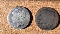 Two Morgan silver dollars side by side on a plain surface showing both obverses dated 1880 and 1899 with worn details.