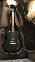 Full-length front view of black SG guitar seated in open hardshell case