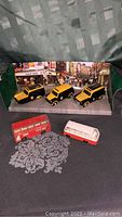 Five vintage Matchbox vehicles displayed on black surface with grey floral pattern; three black and yellow vehicles in green box and two separate buses (red double decker and white/red bus).