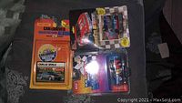 Two NASCAR Muscle Machines cars packaged with Car-Driver collector card album and Matchbox Cadillac Seville car on a dark surface.