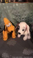 Photo of two Disney plush stuffed animals, Goofy and Dalmatian, on a patterned cloth background.