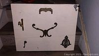 White wooden coat hanger rack with multiple antique brass and iron hardware pieces mounted for hanging items.