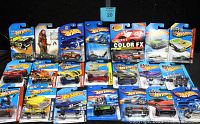 Photo showing all 20 Hot Wheels cars in original packaging arranged together, highlighting the variety including the Color FX Ferrari and Justice League themed cars.