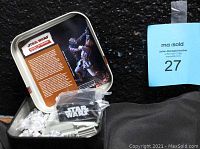 Opened tin showing unassembled pewter pieces, display stand in plastic bag with Star Wars logo, informational card with Duel scene image inside lid.