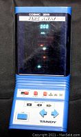 Close-up front photo of the Tandy COSMIC 2000 FIRE AWAY handheld electronic video game powered on showing gameplay and controls.