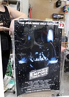 Full view of the laminated Star Wars The Empire Strikes Back poster held by a person showing the black background with Darth Vader image and white title text.