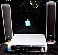 Front view photo showing the Toshiba CD changer unit and two speakers, all placed against a black wall background.