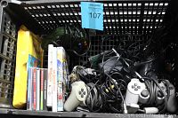 Plastic tote with multiple wired white and black video game controllers, game cases aligned upright, and accessory cables tangled