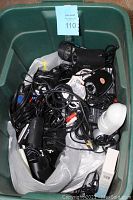 Top-down view of green tote filled with black wired security cameras, cables, and a white motion sensor device showing condition and contents