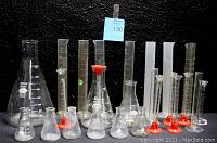 Front view showing assorted sizes of glass and plastic beakers and graduated cylinders arranged from tallest to shortest.