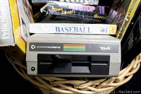 Commodore 1541 disk drive with software boxes including Championship Baseball and Pit Stop behind it in basket.