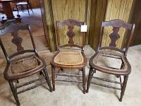 Three antique wooden cane chairs shown together, two with damaged cane seats and one intact.