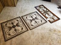 Three decorative metal wall art pieces on carpet with two square matching panels and one rectangular panel.