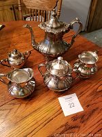 Photo showing the entire silver-plated tea set on wood table, including coffee pot, sugar bowls, and creamers.