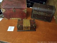 Three decorative treasure chest style wooden boxes on a wooden table, showing size and color differences.