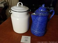 Overview of the two enamelware items placed on a wooden table: the white canister and the blue coffee pot.