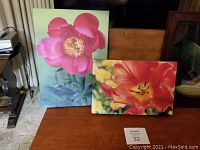 Two floral canvases standing side by side, one 14x10 inches with a bright pink flower and one 12x8 inches with an orange-red flower.