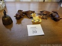 Lot of four Asian decorative items including two wooden koi fish, bronze bell, and porcelain dog figurine on wooden table.