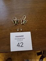 Photo showing two pairs of earrings: butterfly-shaped dangle earrings with colorful inlay stones and simple silver studs, placed on a wooden surface with auction tag