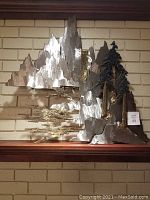 Front view of full metal sculpture against brick background, showing mountains, trees and flowing water design