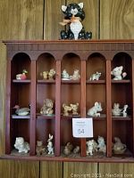 Front view of wooden wall curio cabinet containing multiple small vintage porcelain animal figurines in separate vertical sections.