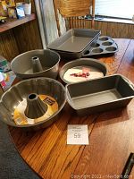 Photo showing all bakeware pieces on wooden table including two rectangular baking pans, loaf pan, two round cake pans, fluted tube pan, and tube cake pan.