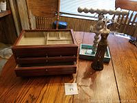 Wood and glass jewelry box with two wooden jewelry stands on a wooden table in sunlight