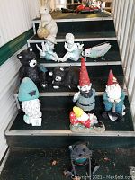Overall view of 11 yard art pieces arranged on stair steps including ceramic gnomes, bears, fairies, metal grasshopper and metal cat sculpture.