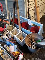Photo showing lot contents including toolbox with tools, two red planter boxes on white frame, bucket with hand tools, new broom, dustpan, and other miscellaneous tools.