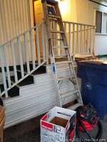 Image of an 8-foot aluminum ladder leaning against mobile home stairs with a red and black 5-gallon Shop-Vac vacuum on ground near an open Shop-Vac box.