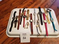 Top view of 16 women's wristwatches on a white tray showing variety of bands and faces.