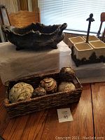 Photo showing the gothic-style stoneware centerpiece on cast iron base napkin holder and the woven basket with decorative balls on a wooden table.