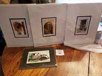 Three 11x14 art prints with European doorway themes standing upright on a table, unframed but matted.