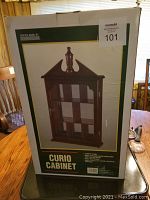 Photo of boxed curio cabinet showing box with product image and MaxSold lot tag.