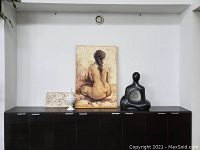 Full view of all four items: Bathing lady painting on canvas, white ceramic cherub relief wall art, white ceramic candy dish with lid, abstract black sculpture.