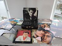 Wide view of the Crosley record player with multiple vinyl records spread around it, featuring various album covers including Bryan Adams and Bobby Rydell.