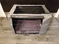 Large black metal wire frame dog crate covered with gray Petsfit fabric cover, with front door open showing inside KONG dog bed.