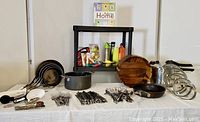 Full overview of lot showing cookware, cutlery, serving bowl, kitchen utensils, water bottles, fresh balls, and cookbook on shelf