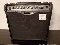 Front view of the Line 6 amplifier showing the black grill, LINE 6 logo in center, and control panel on top.