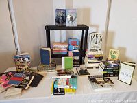 Overall lot of mixed paperback and hardcover books arranged on a table and shelf, showing various titles and genres.
