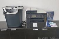Photo showing Canon imageCLASS MF4880dw and Fellowes shredder side by side with manuals and CDs on a black cabinet.