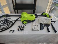 Main steamer unit in lime green and dark gray with hose, pistol-grip wand, two extension wands, microfiber floor brush, user manual and assorted brush heads laid out on table.