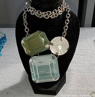 Close-up photo of a large chain-link necklace with three large faceted stones in green, clear, and silver