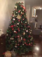 Front view of the 7ft artificial Christmas tree showing red, gold, white, and green ornaments, gold ribbons, and integrated white lights.